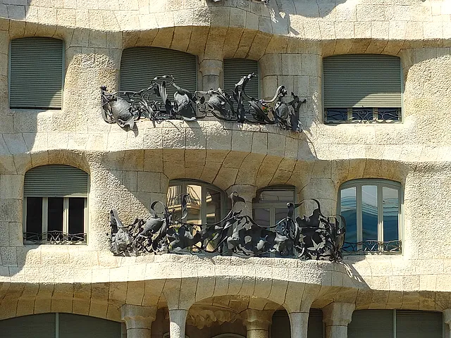 Two floors of Casa Milà with balcony railings of twisted wrought iron set against the pitted stone wall