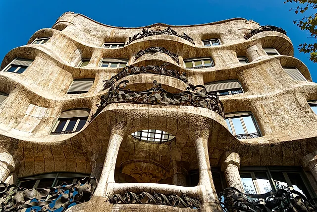 Looking up at the corner of Casa Milà: the rippling stone walls, the wide window openings and the dark iron balconies against a blue sky